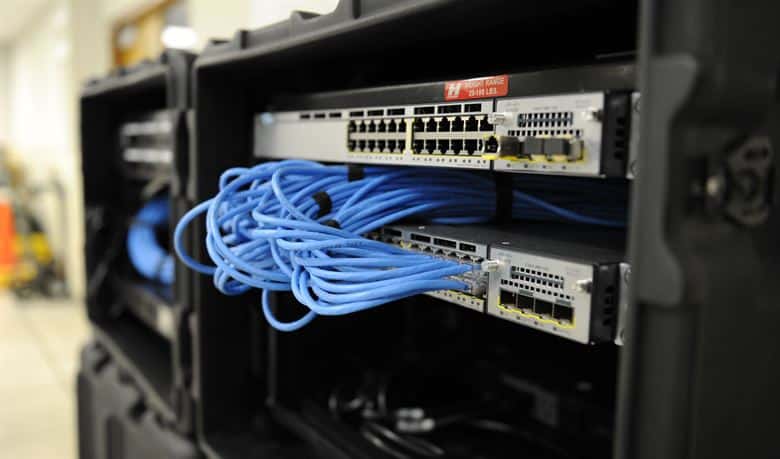 Shows a black cabinet with network switches and blues cabling